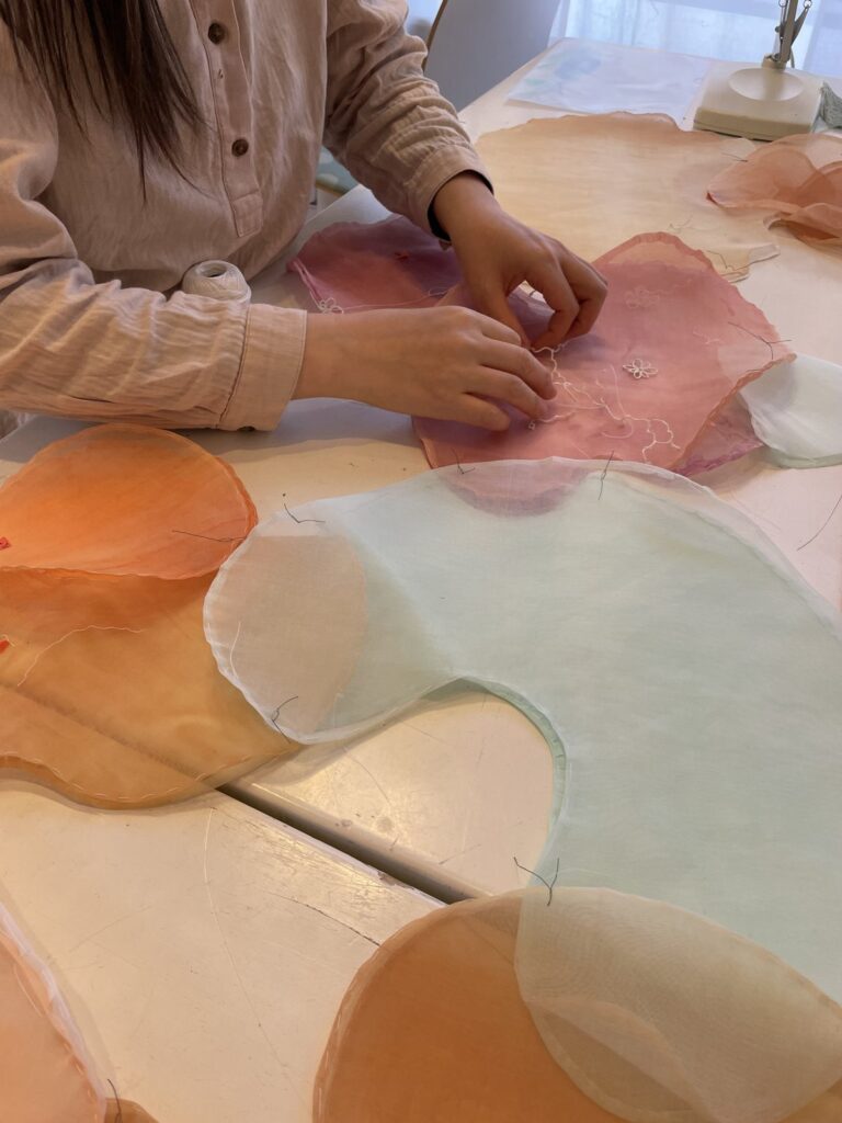 Händer arbetar med rundade former i rosa, orange och ljusblå textil i Hazuki Fukutas konstsömnadsarbete.