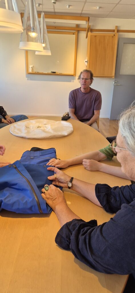 Studerande känner på ett blått tyg under ett samtal kring bordet hos FOV Fabrics.
