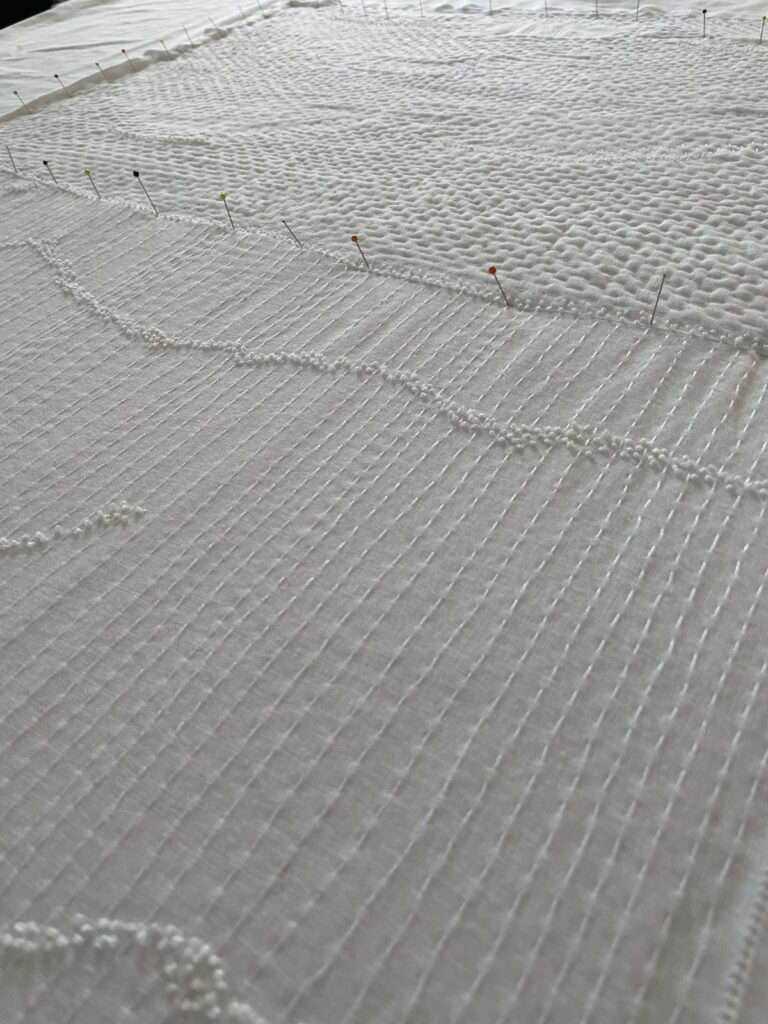 Närbild av vitt konstsömnadsarbete med täta stygn, struktur och geometriska fält.